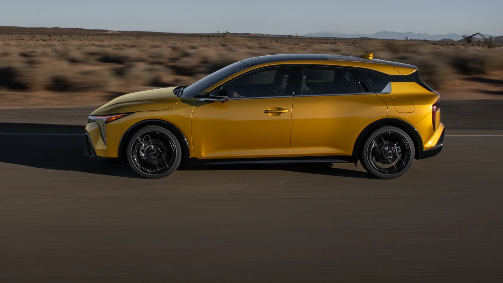 Kia K4 à hayon 2026 jaune vue de profil sur une route dégagée, collines en arrière-plan.