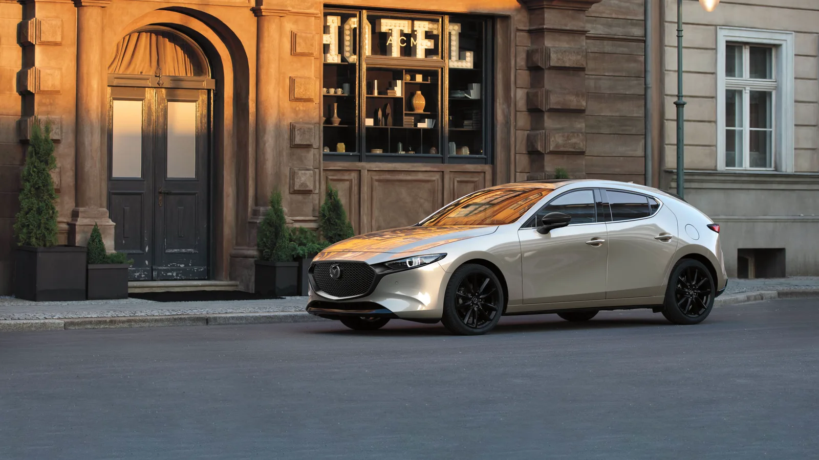 Mazda3 Sport 2026 beige vue de trois quarts avant dans une rue pavée, devant un hôtel.