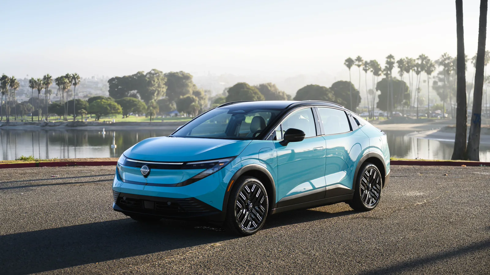 Nissan LEAF 2026 turquoise vue de trois quarts avant près de l’eau, avec des palmiers à l’arrière-plan.