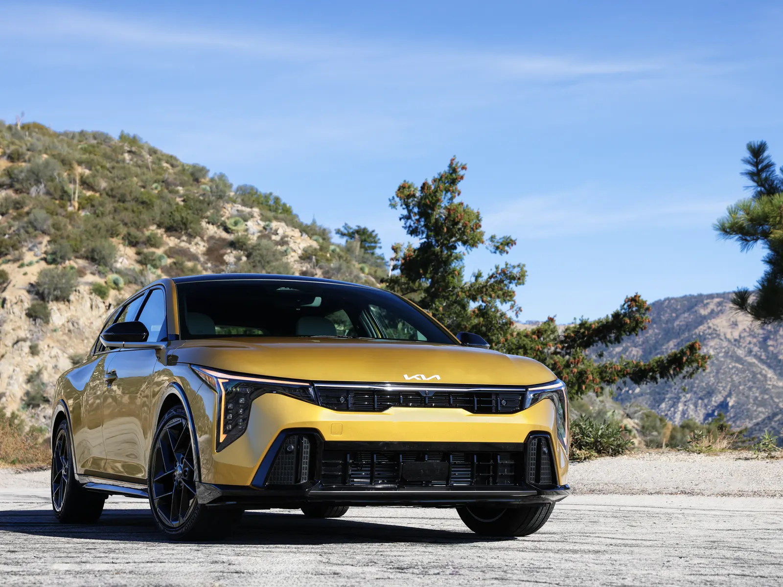Kia K4 à hayon jaune vu de trois quarts avant, en montagne sous un ciel bleu