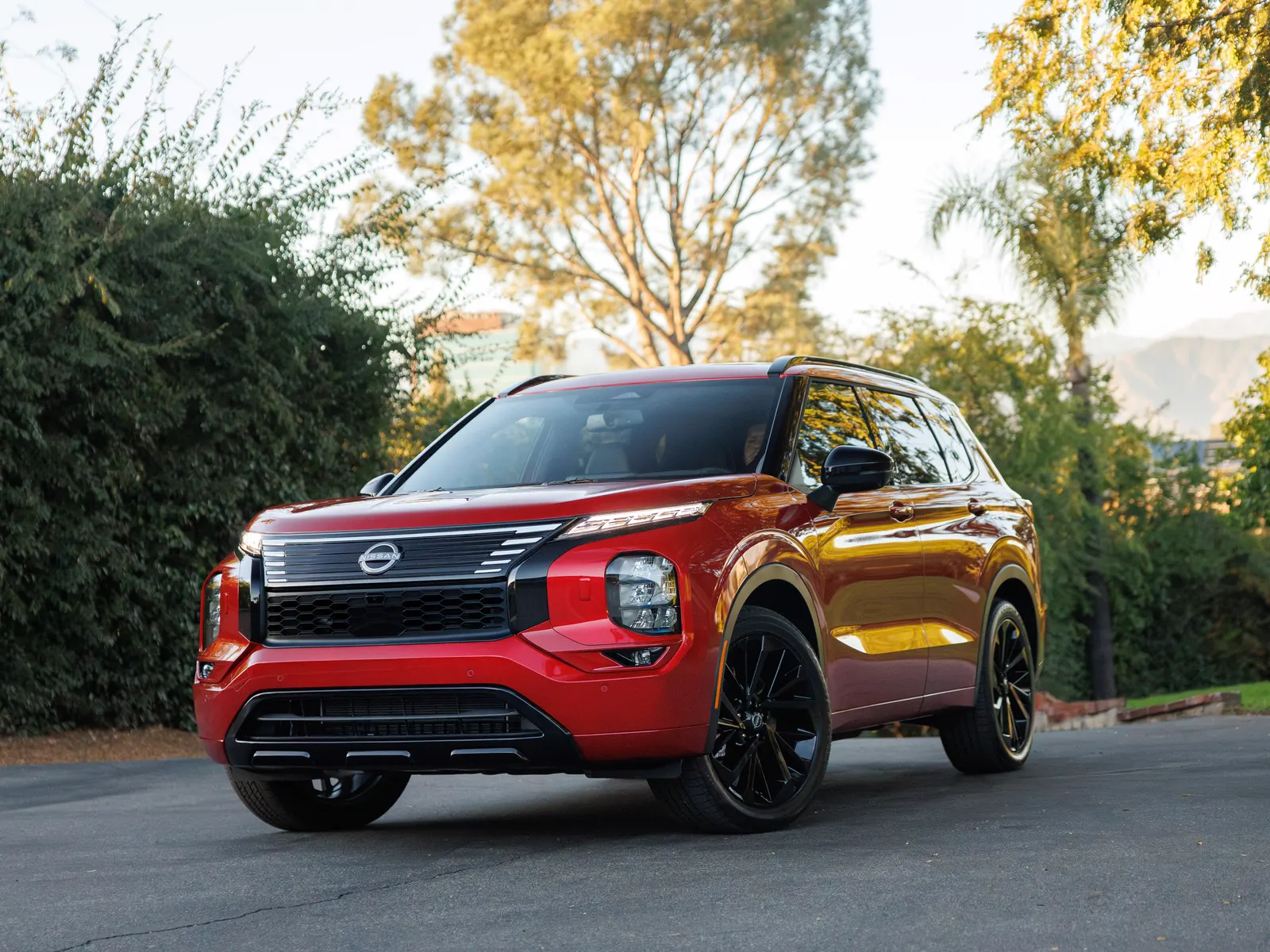Nissan Rogue rouge vu de trois quarts avant au soleil couchant, devant des arbres dorés