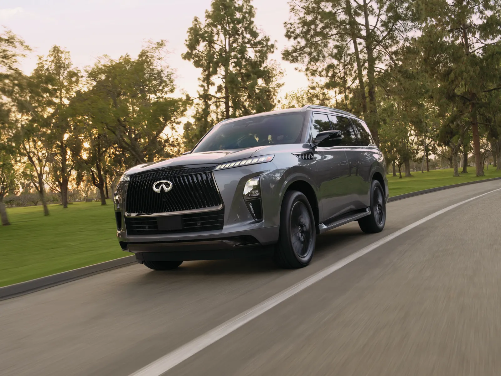 INFINITI QX80 gris roulant sur une route bordée d'arbres, en fin de journée