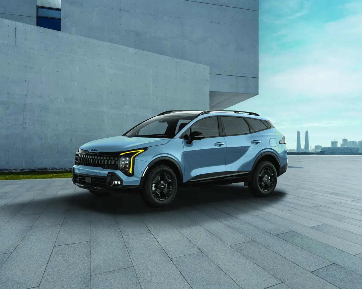 Kia Sportage 2026 bleu pâle vu de trois quarts avant sur une esplanade de béton, ville à l'horizon.
