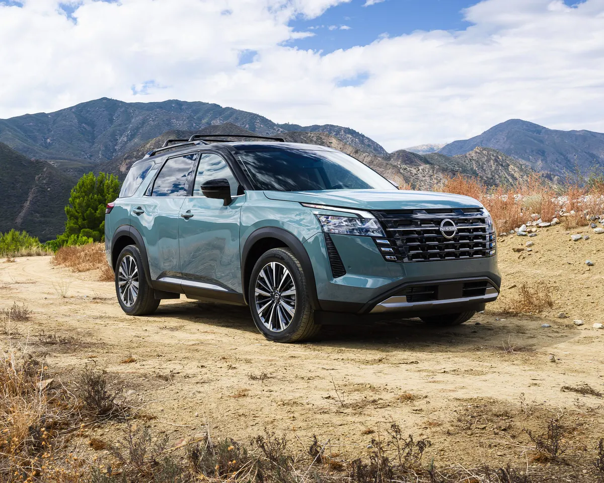 Nissan Pathfinder 2026 vert-de-gris vu de trois quarts avant sur un terrain sec, montagnes en arrière-plan.
